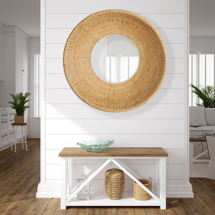 Round rattan wall mirror with deep woven frame styled above a white entryway console in a coastal space