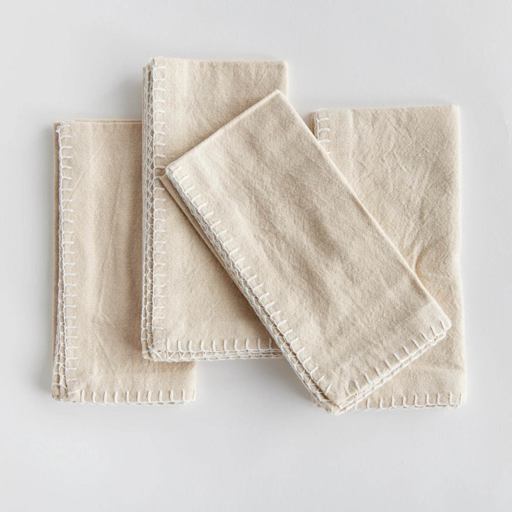 Four taupe cotton dinner napkins shown folded flat with visible whipstitch edging, neutral tabletop styling – Modern Farmhouse.