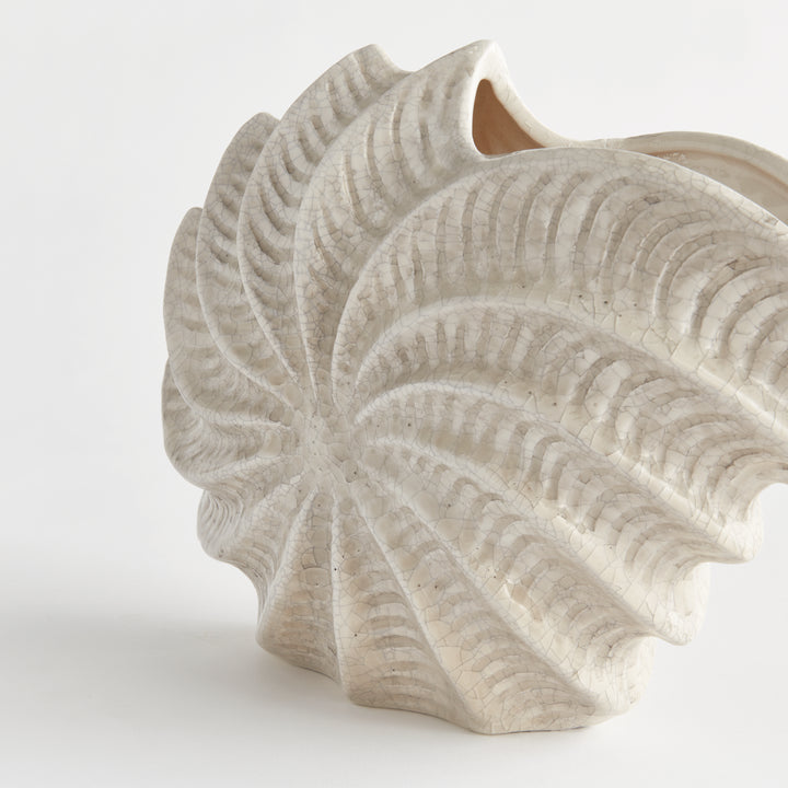Close detail of a cream shell vase showing the spiral ridges and textured relief across its antique glazed clay body. Coastal