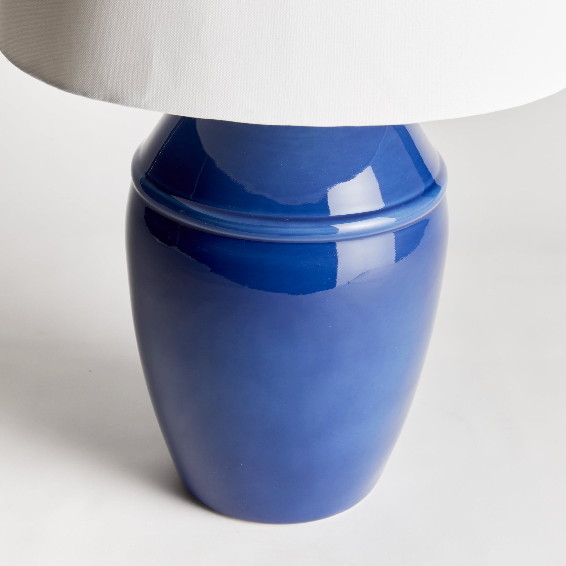 Constructed with a ceramic body and adorned with a deep, luxurious glaze, this coastal-inspired lamp exudes elegance. Enhancing its design, the wide drum shade is crafted from soft white linen, providing a striking contrast. Whether placed on a bedside table, console, or study desk, this lamp is a stunning and practical addition to any space. Its timeless blue and white color combination adds a touch of classic beauty.