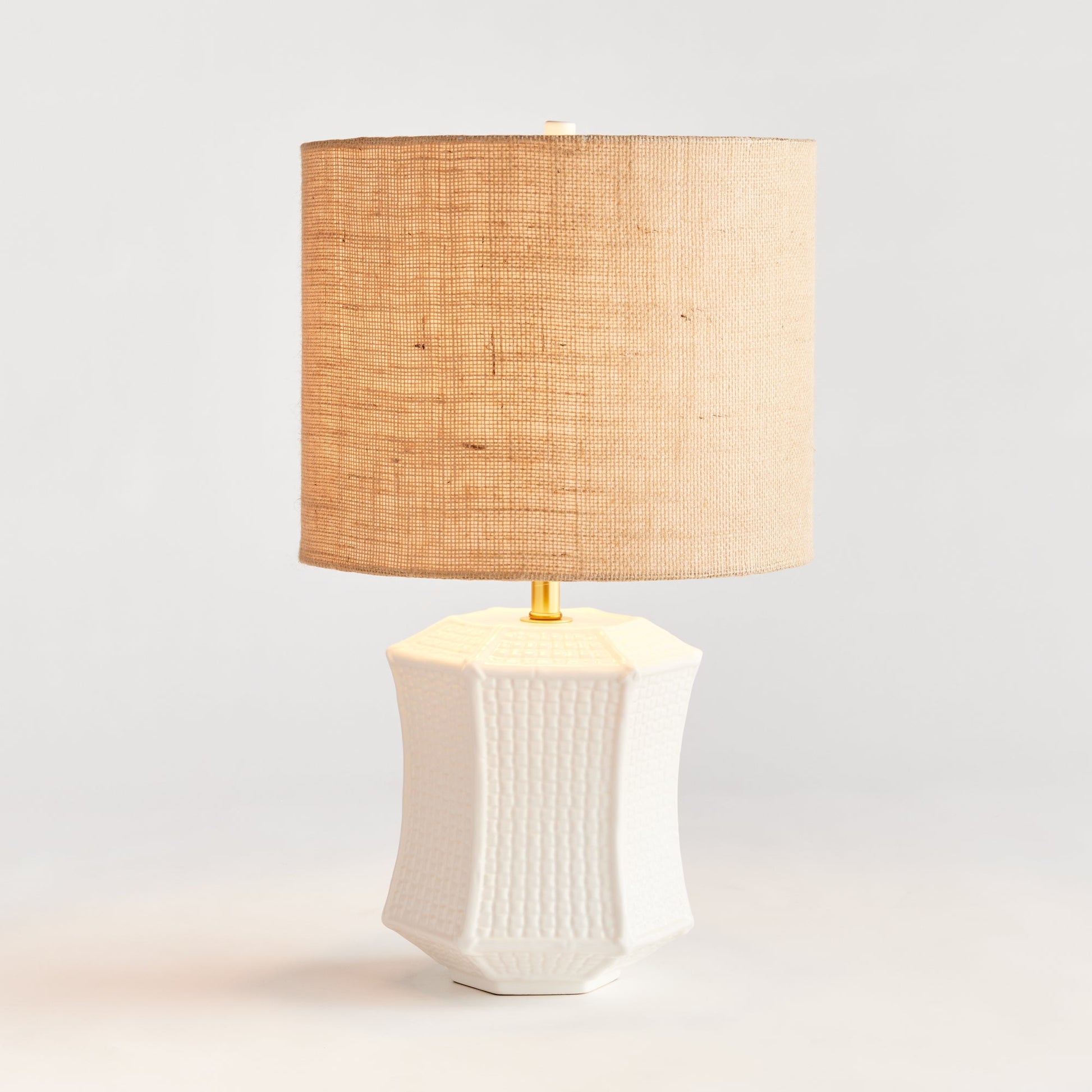 The ceramic base of this table lamp has a unique texture that resembles woven fabric, making it a defining feature of the piece. Its paneled design and impressive size make it a stand-out focal point for any transitional setting. Available in white and tan, this lamp adds an elegant touch to any room.