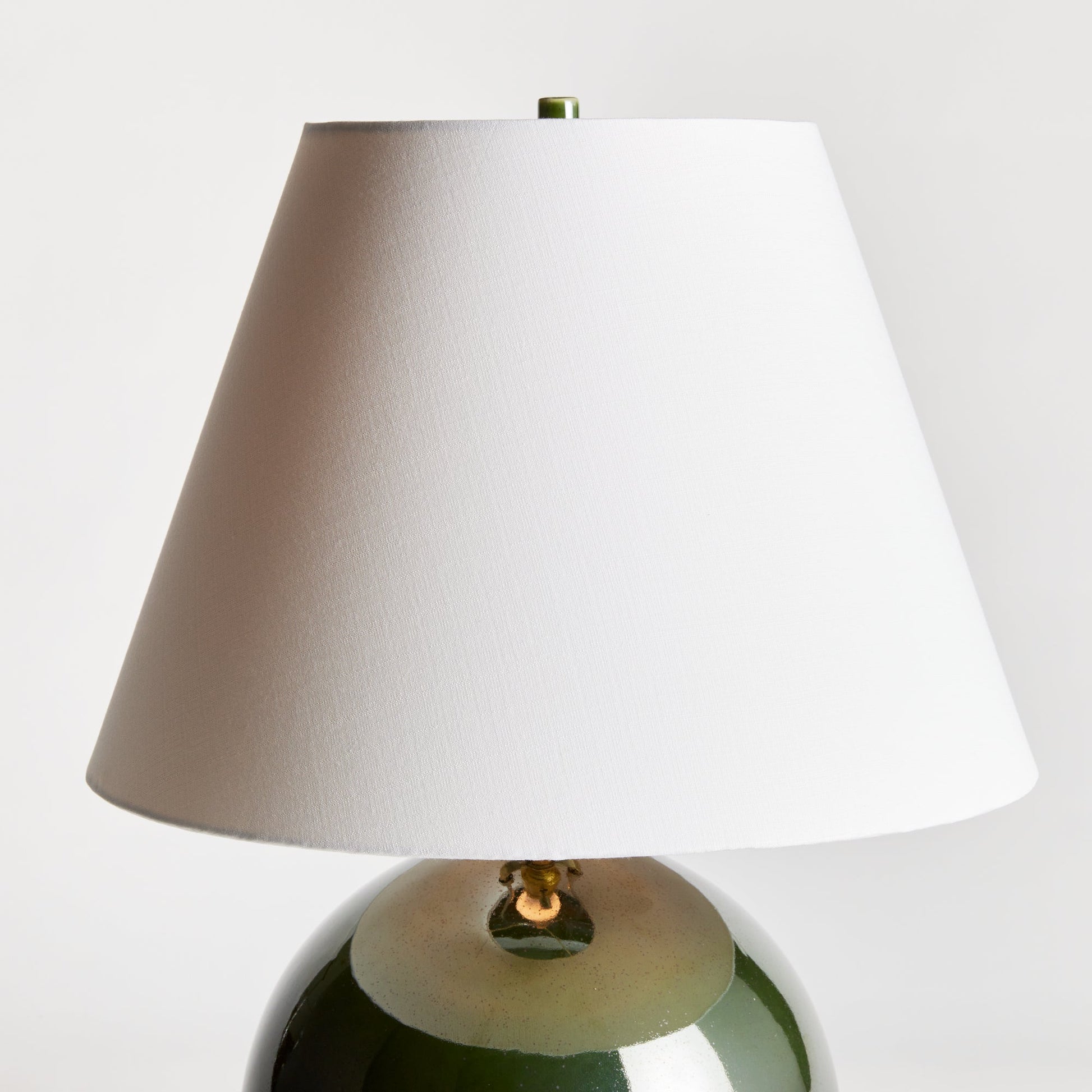 With a perfectly rounded ceramic body and a rich green high gloss glaze, this lamp adds a pop of color to any setting. Topped off with a bright white tapered shade, it makes a lovely accent for bedside table, side table or desk. Expertly crafted with a perfectly rounded ceramic body and a rich green high gloss glaze, the Bellamy Green Table Lamp is a stunning addition to any room