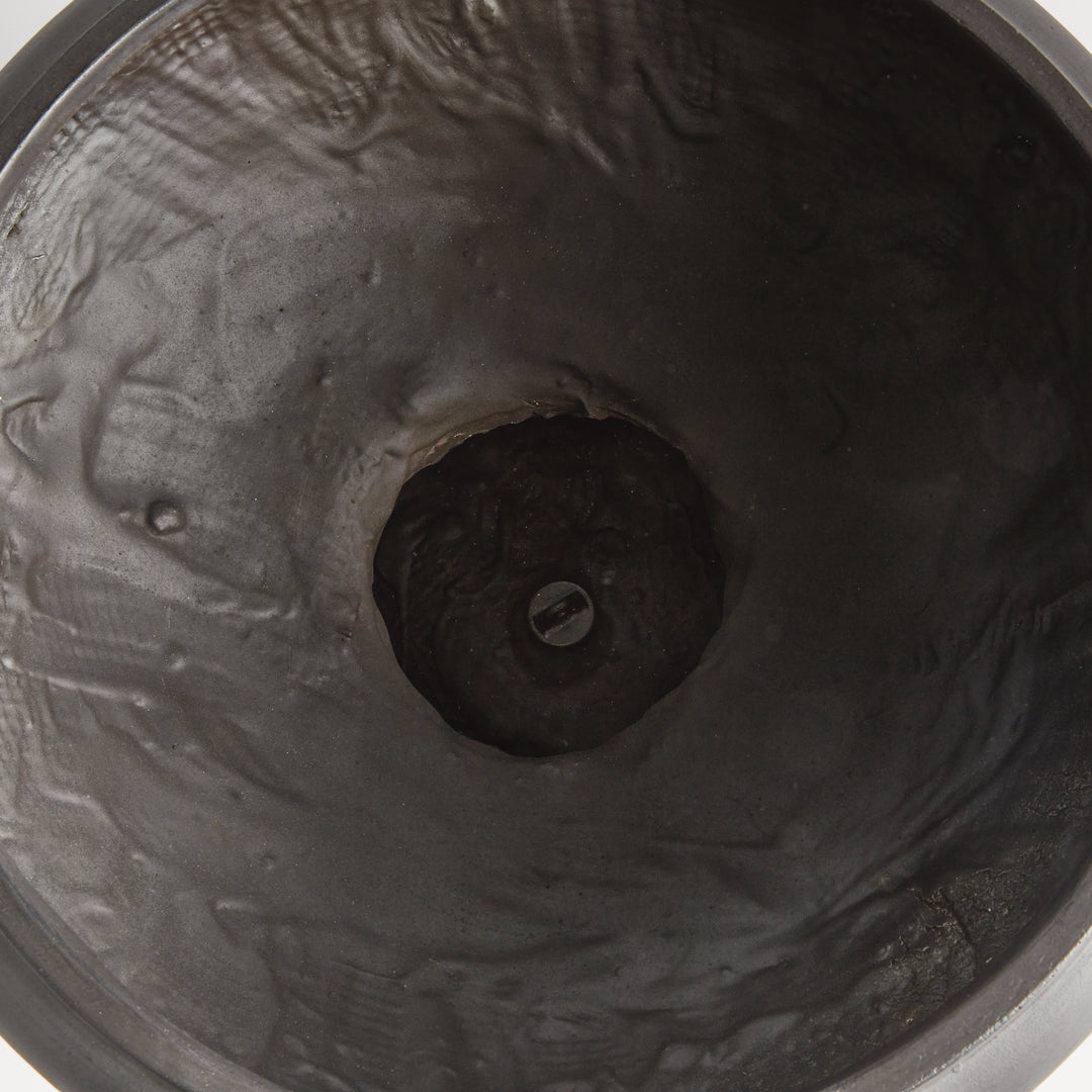 Interior view of an antique black footed bowl planter showing its textured basin and a drain plug at the center. Transitional