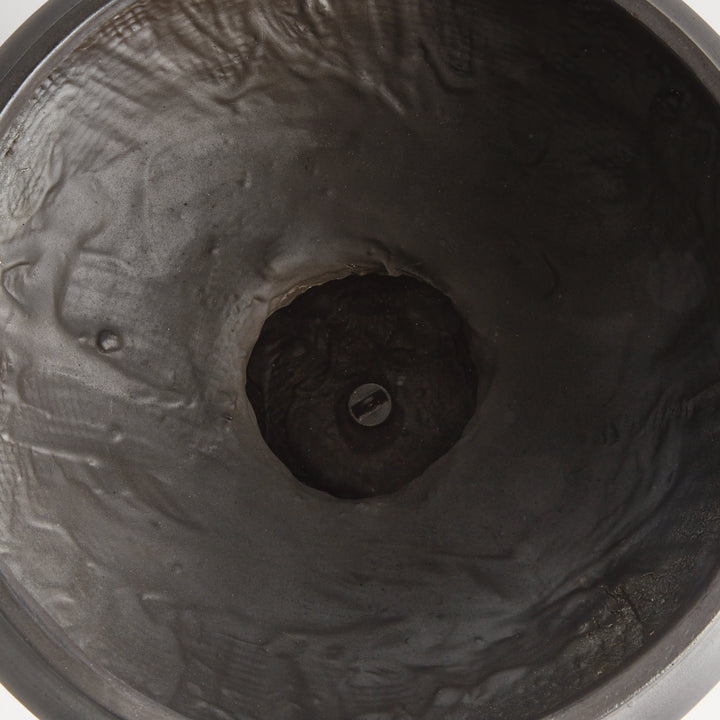 Interior view of an antique black footed bowl planter showing its textured basin and a drain plug at the center. Transitional