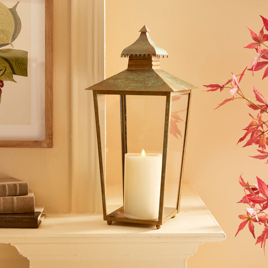 This lantern's design is characterized by a curved pagoda and a notched edge, adding to its simple yet distinctive look. The warm patina finish gives it a weathered appearance, making it a suitable choice for any indoor setting.