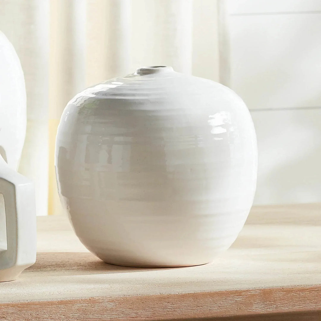 Small oatmeal stoneware vase displayed on a wooden surface beside a window, with its rounded body unfilled | Modern Organic