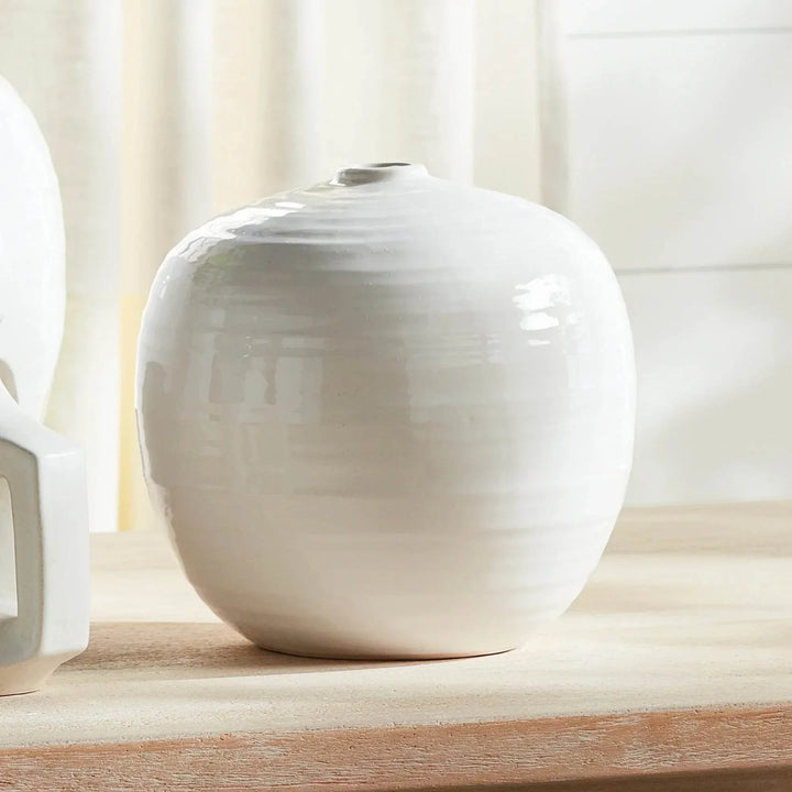Small oatmeal stoneware vase displayed on a wooden surface beside a window, with its rounded body unfilled | Modern Organic