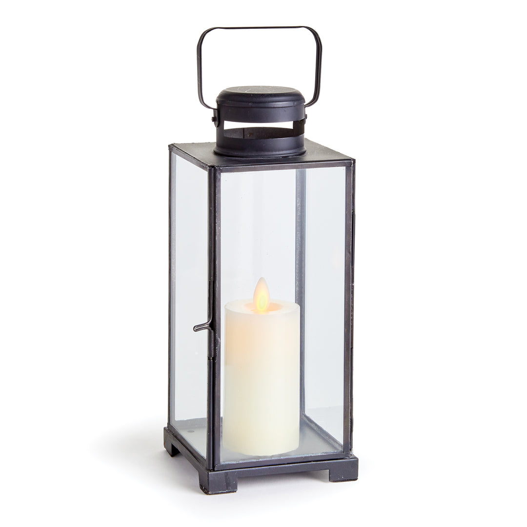 Emmett antique black iron lantern with clear glass panes, a top handle and a candle against a pale background. Transitional