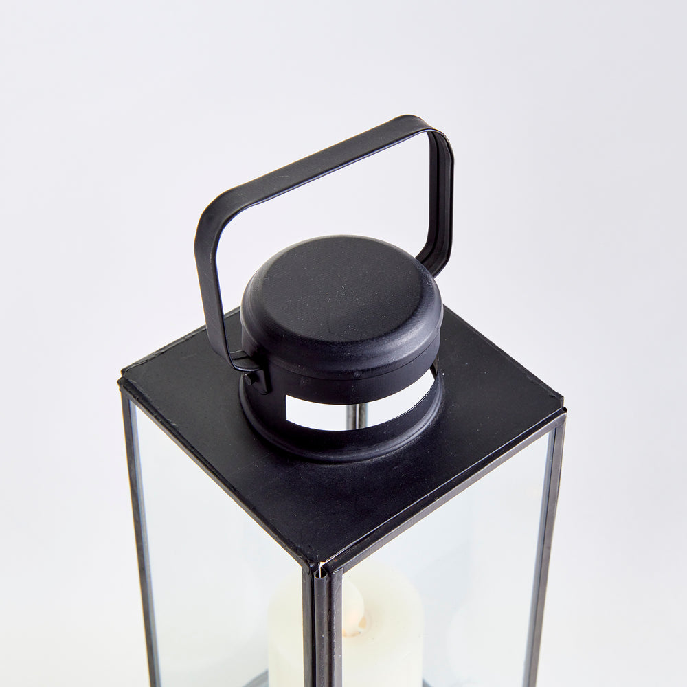Close view of Emmett black lantern showing the top handle, vented cap and clear glass panes on a background. Transitional