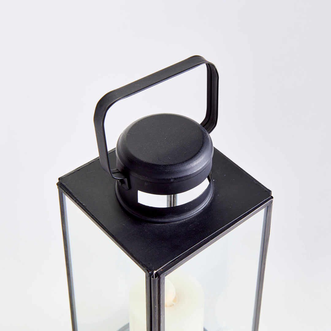Close view of Emmett black lantern showing the top handle, vented cap and clear glass panes on a background. Transitional