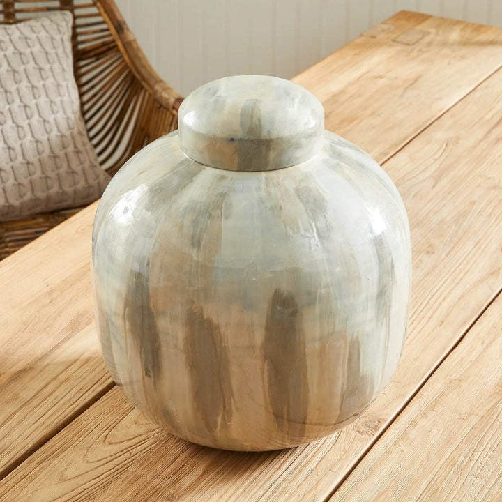 Neutral cream and taupe enameled iron lidded urn, rounded ginger-jar shape and dome lid, shown at an angle on tabletop vignette – Transitional