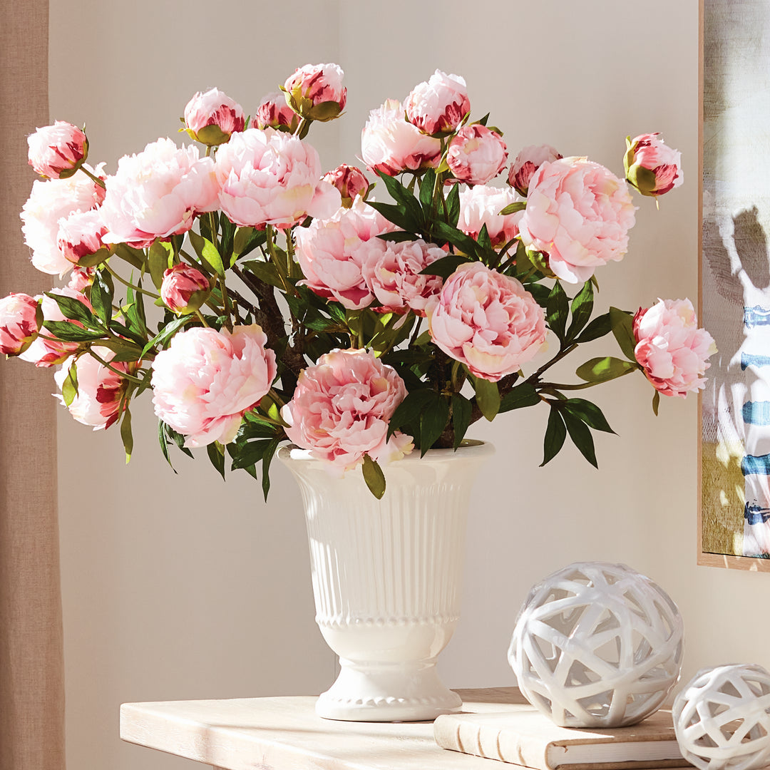 White fluted pedestal vase filled with pink faux peonies, displayed beside white lattice orbs on a console | Traditional