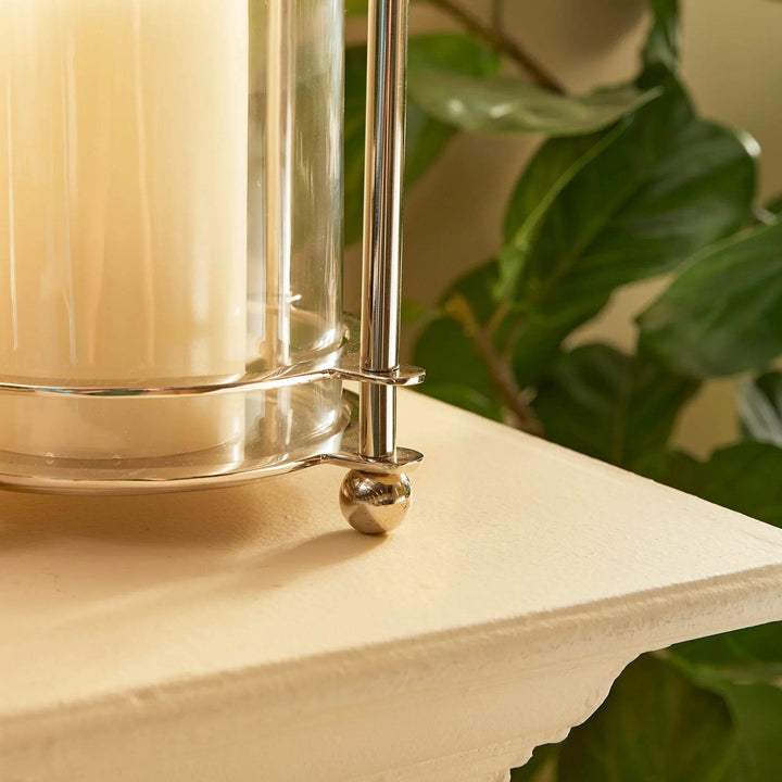 Chrome ball-foot base and clear glass of hurricane candle holder styled with pillar candle
