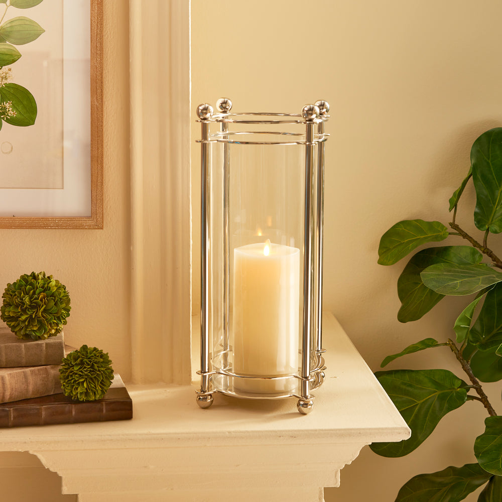 Extra tall chrome hurricane candle holder styled on mantel beside greenery and books