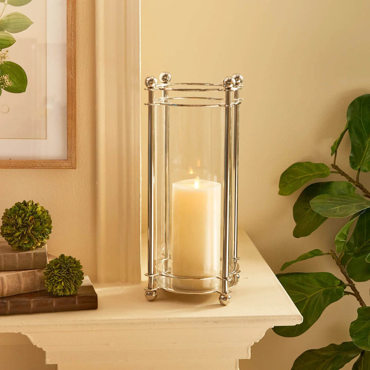 Extra tall chrome hurricane candle holder styled on mantel beside greenery and books