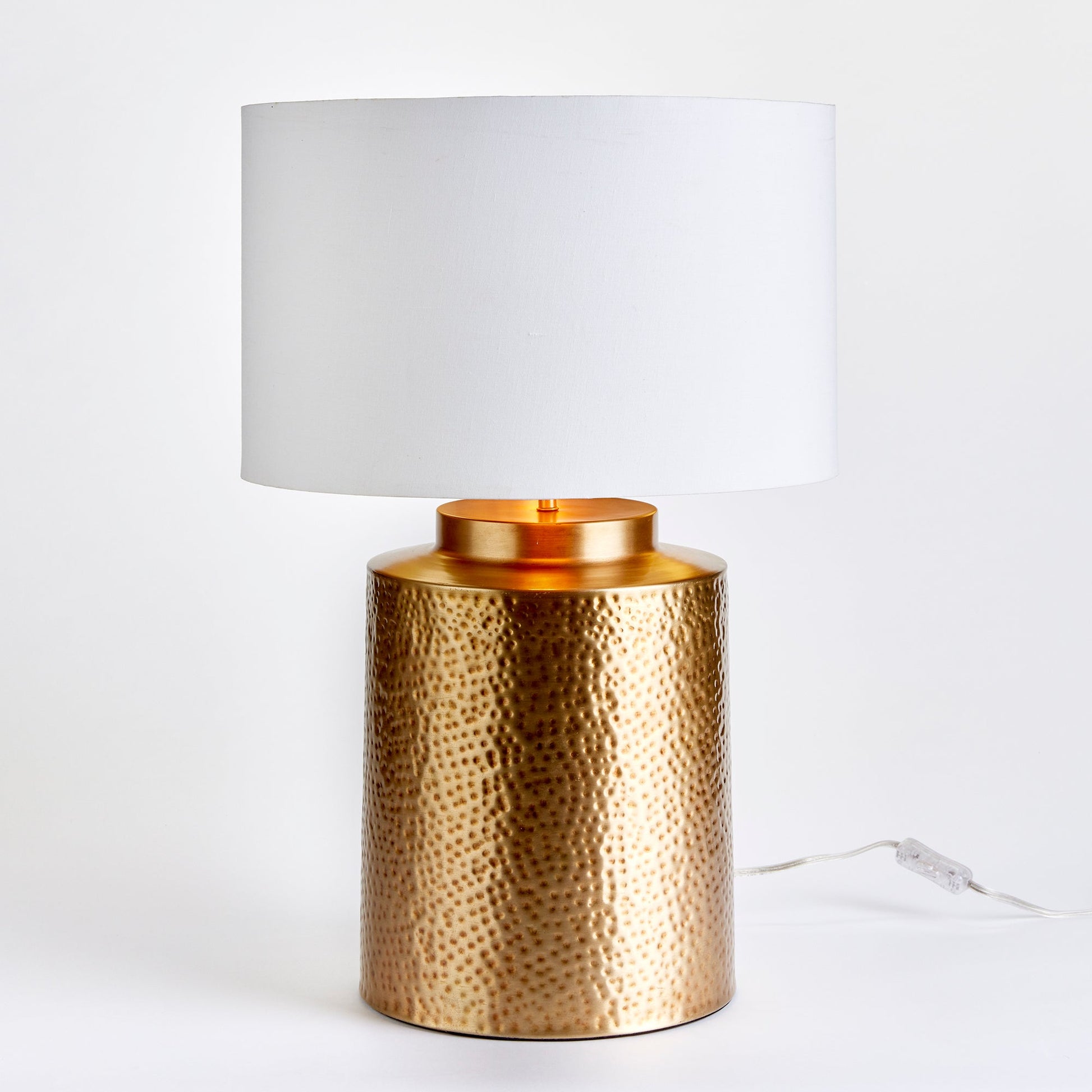 The Keegan Brass Table Lamp makes an impressive statement with its textured brass base and generous size, making it the perfect centerpiece for any space. The bold contrast is heightened by the white gallery shade with a gold inner shade, resulting in a striking and dramatic effect. Expertly crafted with intricate hammered detailing, this lamp is perfect for any living room, table, or living area.