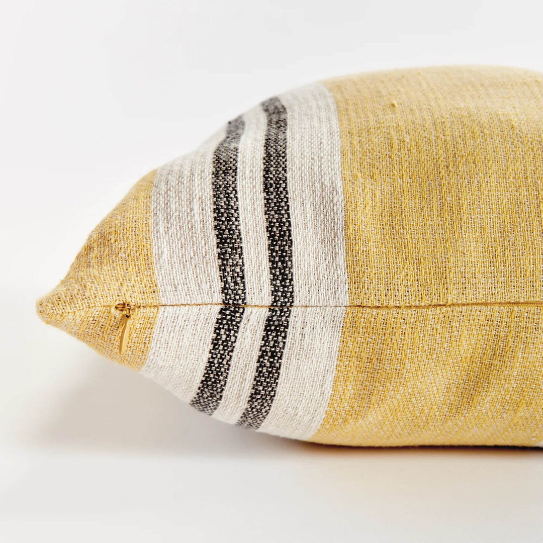 Lifestyle: 24-inch flax linen striped pillow in ochre and charcoal styled on cream sofa with coastal view – Modern Boho.