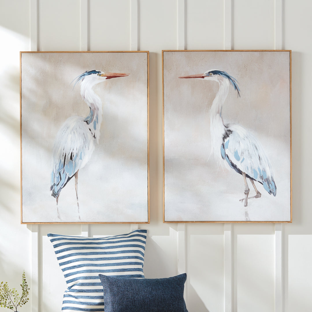 Two framed heron canvas giclee prints displayed together above blue and white upholstered seating area, Coastal Transitional