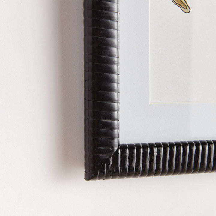 Close-up of rattan-wrapped black frame corner detail on fruit botanical wall art print with glass cover and white matting.