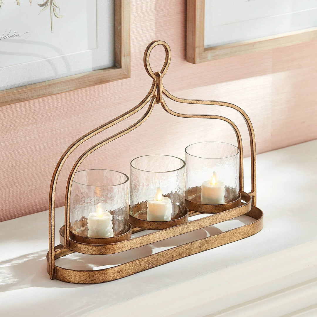 Gold 3-candle hurricane holder with hammered glass cylinders styled on console table, antique gold iron frame with loop handle – Transitional