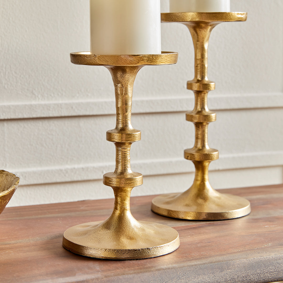 Angled view of gold aluminum pillar candle holders with sculptural stacked spindle profile – Transitional