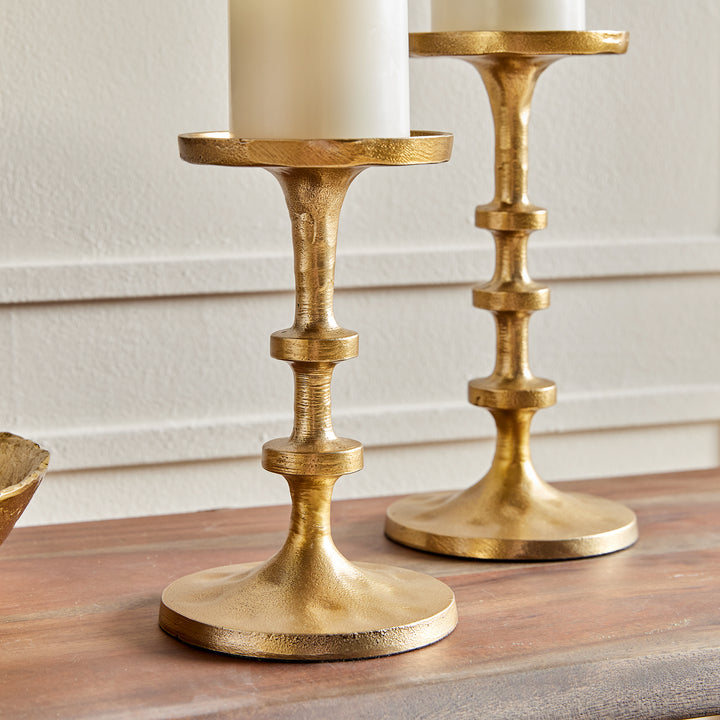 Angled view of gold aluminum pillar candle holders with sculptural stacked spindle profile – Transitional