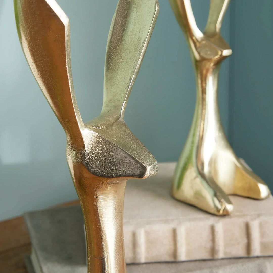Decorative gold jackrabbit figurines styled in a cozy vignette with books and wood surface – Modern Coastal.