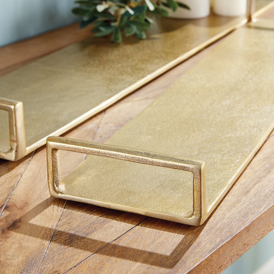 Close-up of long gold cast aluminum decorative trays with textured surfaces and open rectangular handles – Transitional.