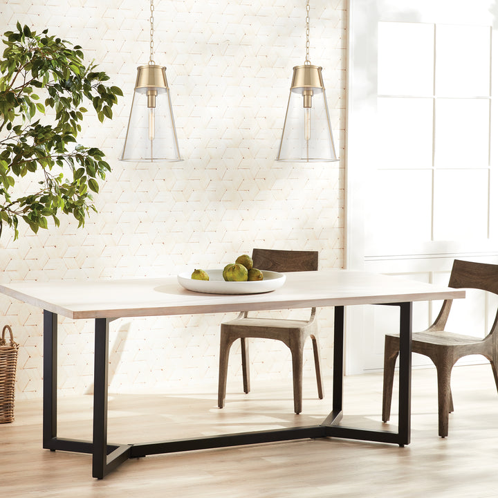 Two gold clear glass pendant lights hanging over a pale dining table beside a wide window and indoor tree, Transitional style