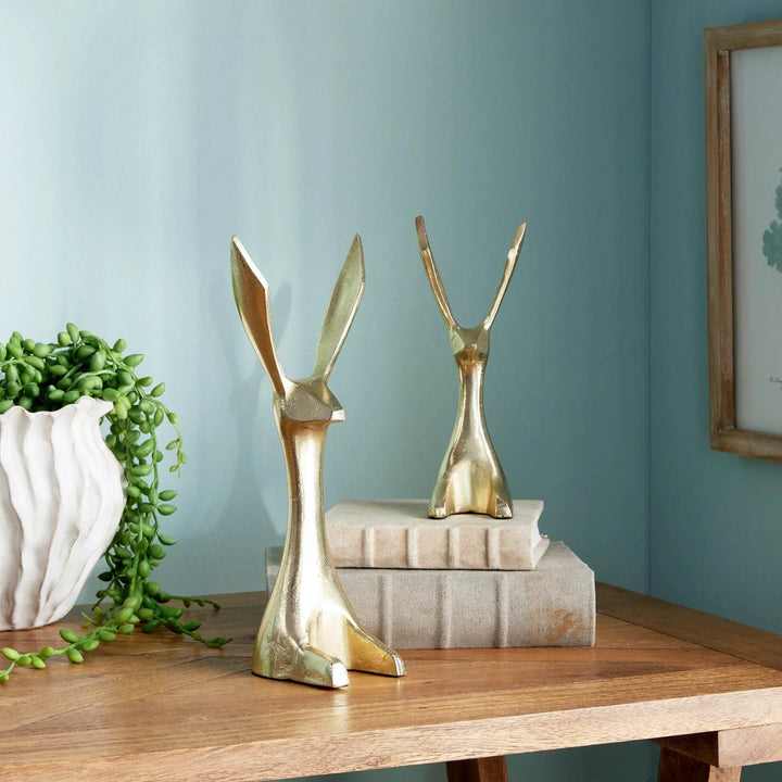 Gold bunny sculptures styled on linen-covered books and wooden table near green plant – Modern Coastal.