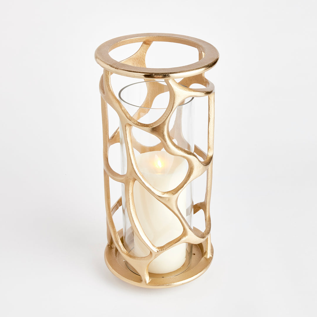 Rear view of gold sculptural hurricane candle holder highlighting the open organic cast aluminum design and glass insert, modern candle holder