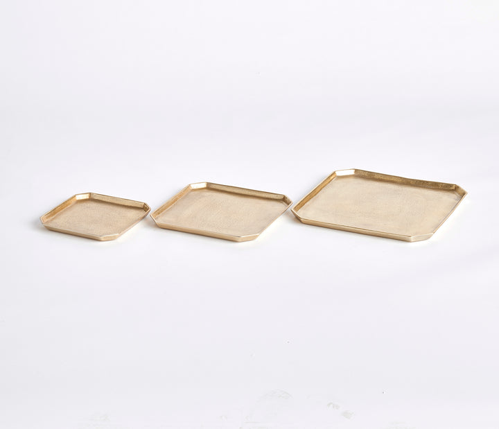 Three gold square cast aluminum serving trays shown from a side angle with shallow raised rims on white, Transitional style