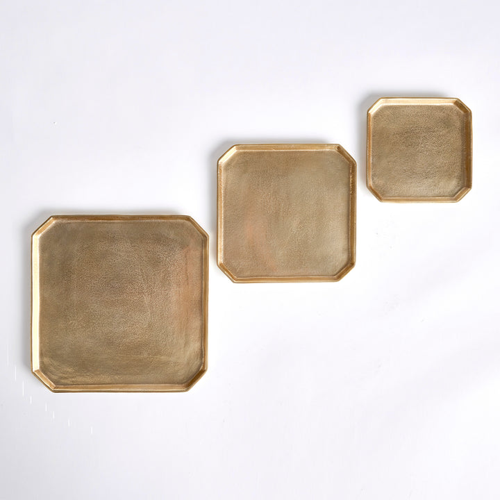 Three graduated gold square cast aluminum serving trays arranged separately in an overhead product view, Transitional style