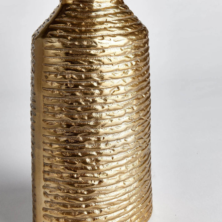 Closeup of banded texture on small gold aluminum vase, showing horizontal ridges and metallic surface


