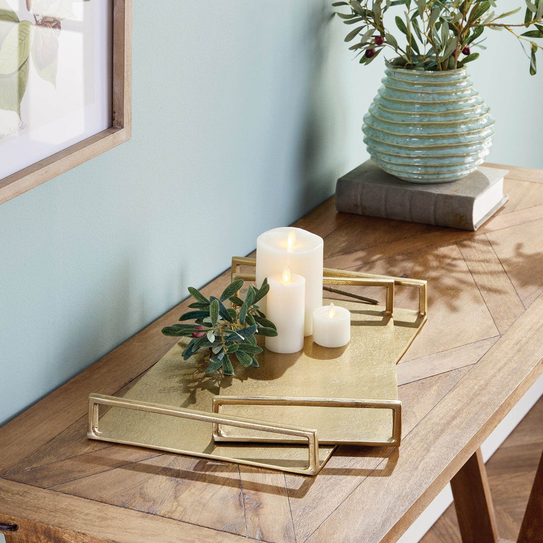 Gold textured decorative trays on a console with candles and greenery, rectangular forms with open handles – Transitional.