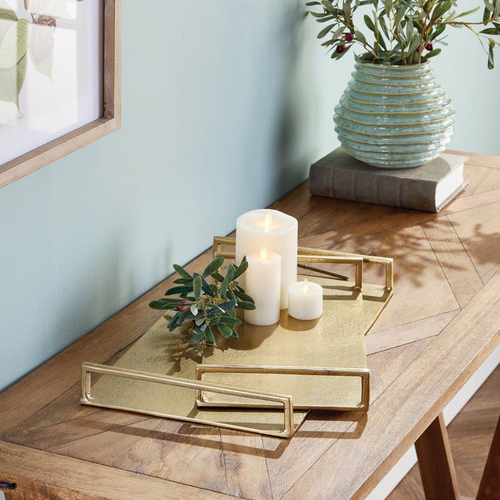 Gold textured decorative trays on a console with candles and greenery, rectangular forms with open handles – Transitional.