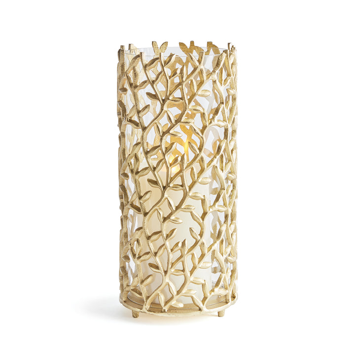 Gold metal hurricane candle holder with vine pattern and glass insert styled for modern botanical luxe interiors.
