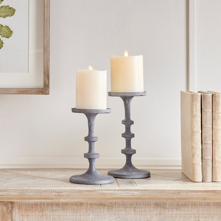 Gray aluminum pillar candle holders styled on a console table with layered decorative accessories – Transitional