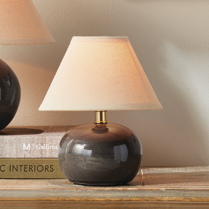 Gray ceramic mini table lamp glowing beside stacked books, with a rounded base and a cream linen shade - Coastal Transitional