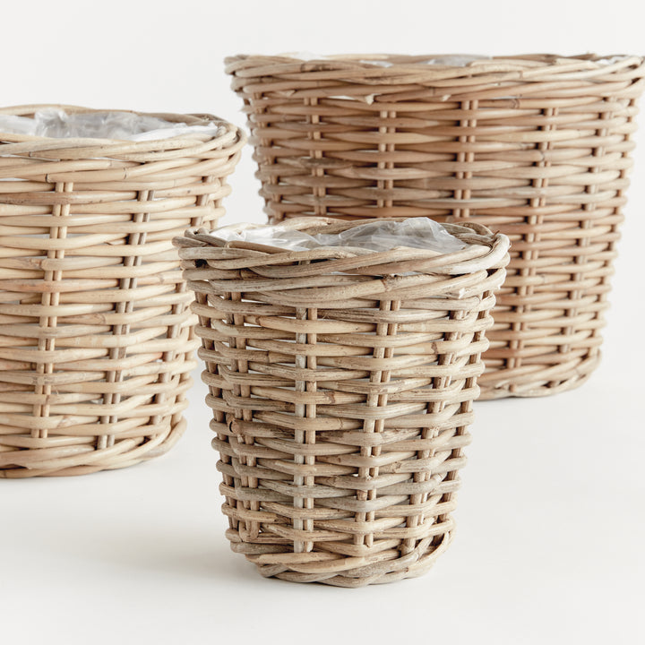 Close view of three tapered rattan basket planters showing the woven sides, thick rims and plastic liners, Modern Farmhouse