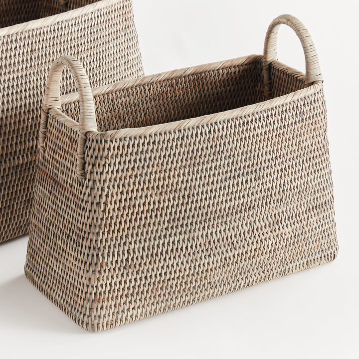 Graywash rattan magazine baskets shown with one in front, revealing the narrow body, woven rim and loop handles, Transitional