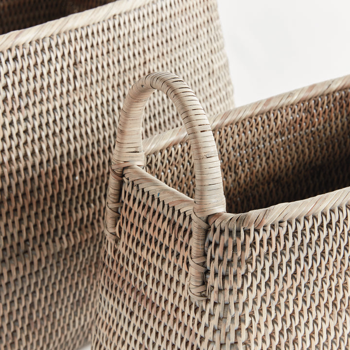 Close view of graywash rattan magazine baskets showing the tight weave, rim and woven loop handle on white, Transitional