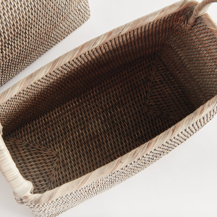 Top view into an empty graywash rattan magazine basket showing the woven interior, narrow body and loop handles, Transitional