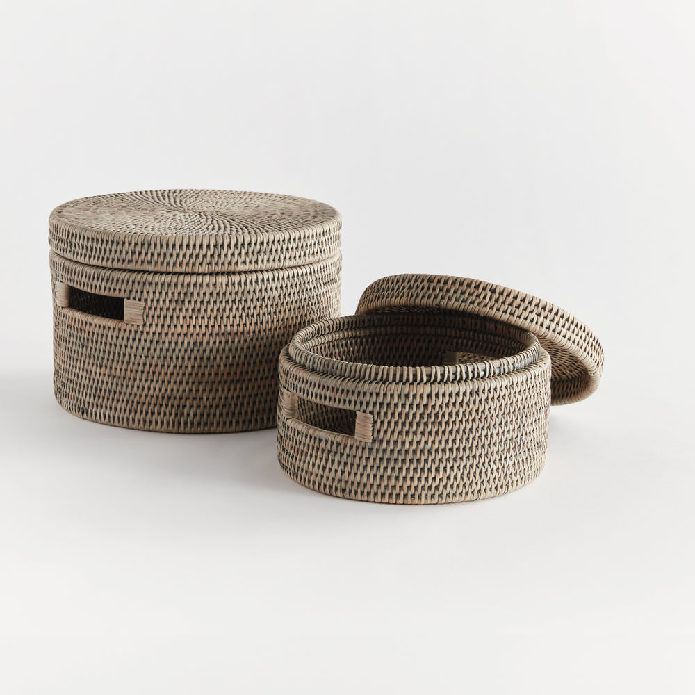 Graywash round rattan boxes with one lid removed, showing the woven interior and graduated sizes against white, Transitional