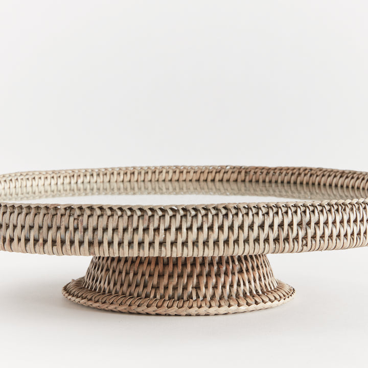 Close view of Hadley graywash rattan stand showing the low pedestal, wrapped circular rim and clear glass insert. Coastal