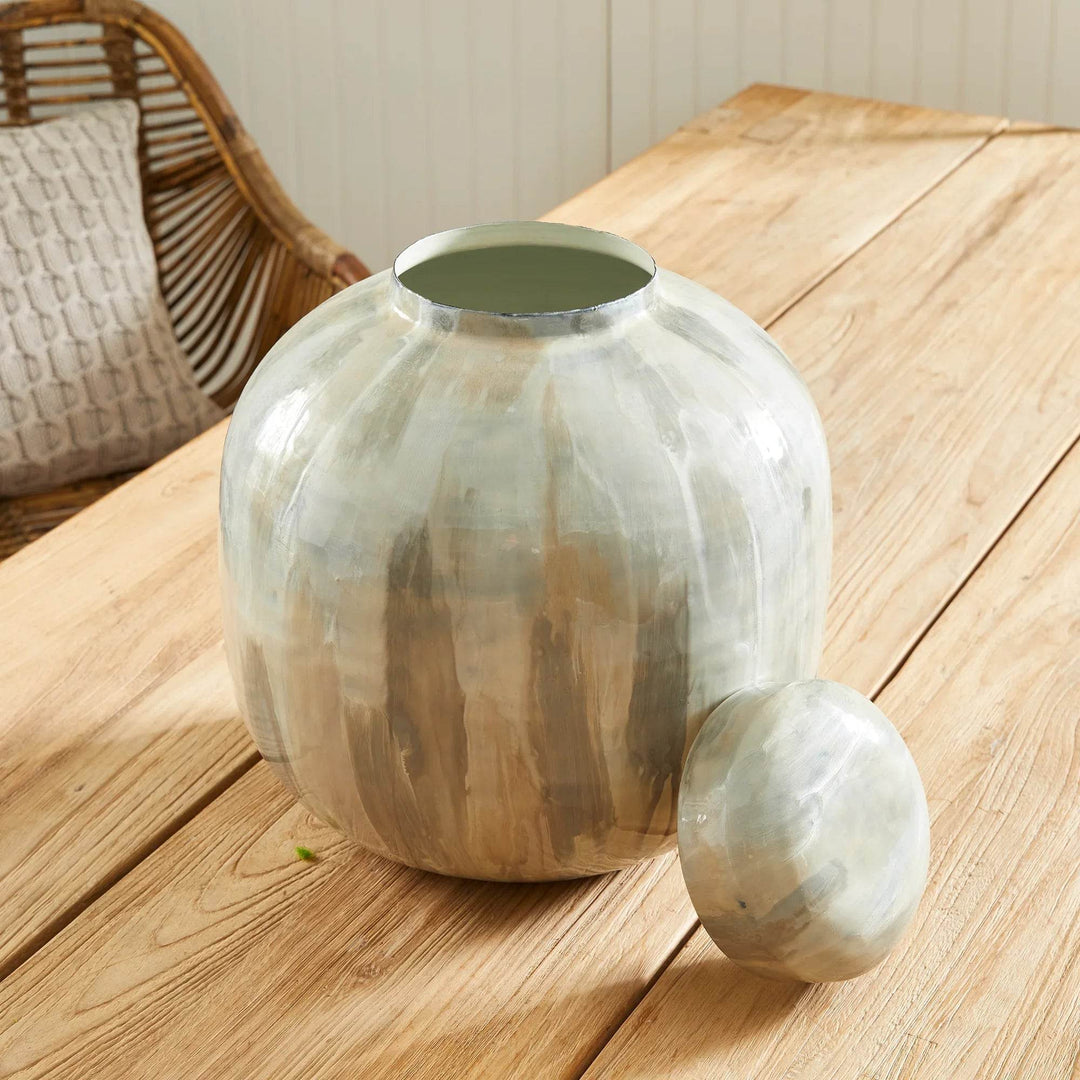 Hand-painted enameled iron lidded urn in neutral cream and taupe with glossy finish, shown on wood table with lid removed beside the opening – Transitional