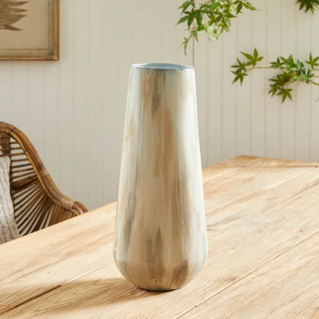 Tall hand-painted enameled iron vase in soft cream and taupe, styled on a wood table with greenery background – Transitional