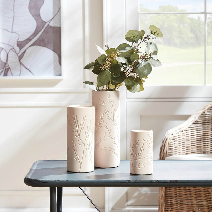 Set of handcrafted beige terracotta vases with vine motif in various sizes, styled on table near window for modern organic decor.

