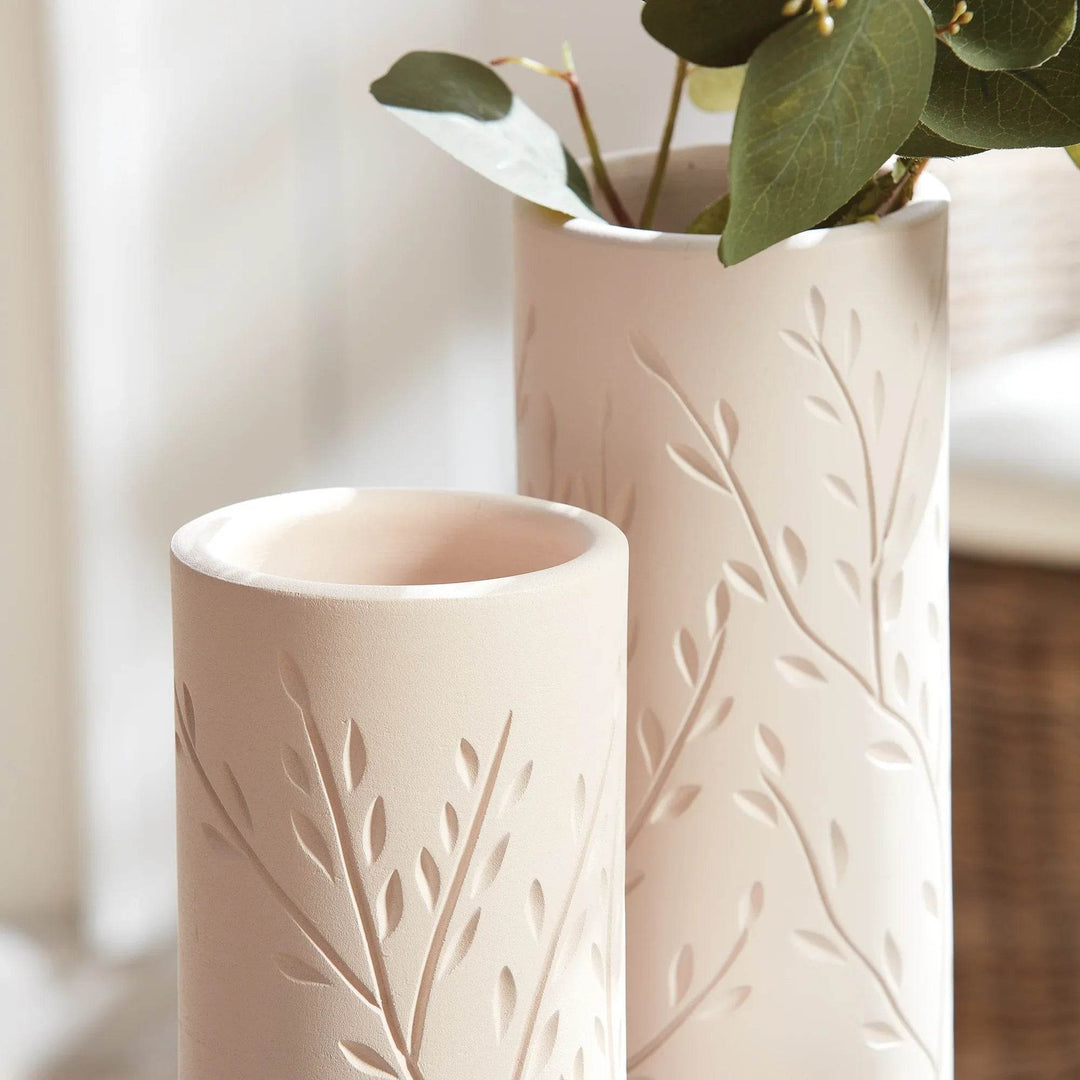 Closeup of handcrafted beige terracotta vases with vine motif, showing carved details and soft matte finish.

