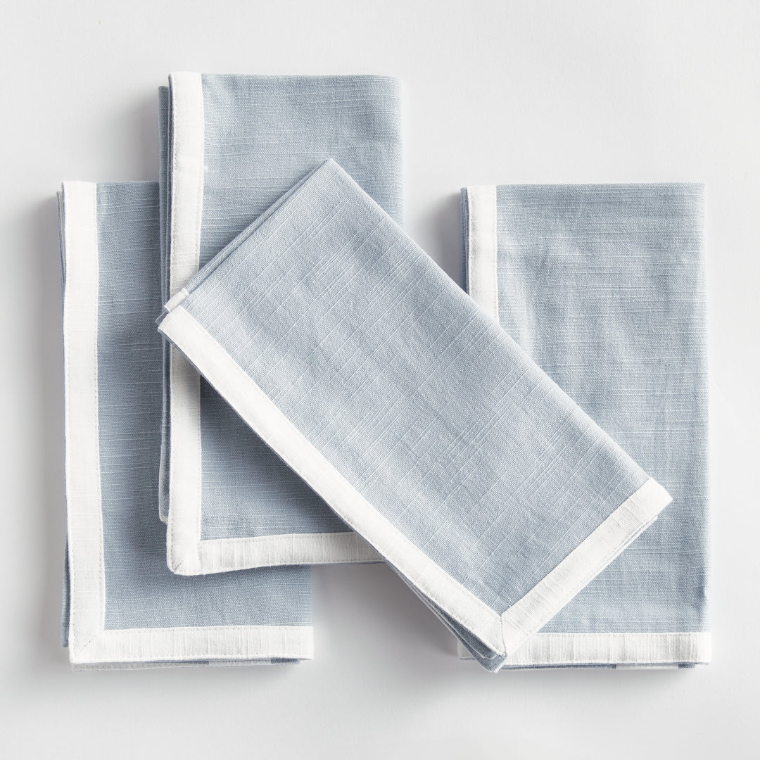 Blue and white dinner napkins, folded in a layered arrangement, showing the border and square cotton fabric. Transitional